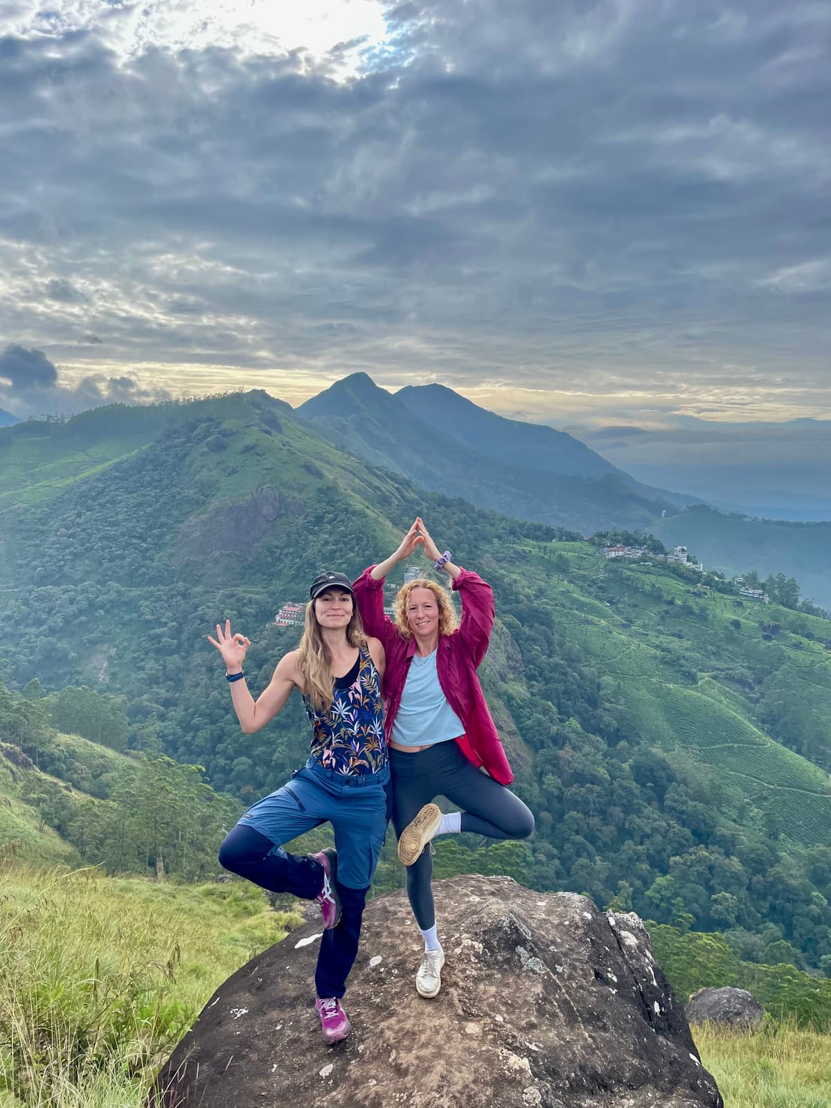 Erika et Astrid en posture de yoga sur un sommet rocheux, vallée verdoyante